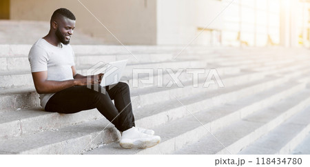 A man sits on a set of stairs outdoors, working on a laptop computer. A man sits on a set of stairs outdoors, working on a laptop computer. 118434780