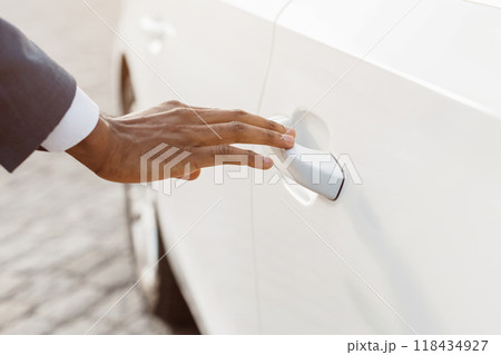 A closeup image of a hand reaching for the door handle of a white car. The hand is in the foreground, and the car door is in the background. The hand is reaching for the door handle A closeup image of a hand reaching for the door handle of a white car. The hand is in the foreground, and the car door is in the background. The hand is reaching for the door handle 118434927