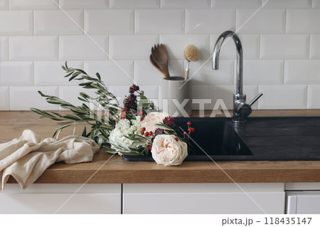 Modern kitchen, Scandinavian interior. Pink roses flowers, olive, rose hips and eucalyptus branches in black sink. Wooden countertop. Eco dish washing concept. Blurred white wall, metro tiles Modern kitchen, Scandinavian interior. Pink roses flowers, olive, rose hips and eucalyptus branches in black sink. Wooden countertop. Eco dish washing concept. Blurred white wall, metro tiles 118435147