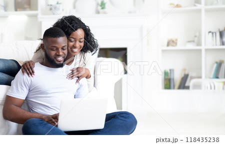 A couple sits on the floor in their living room, the man using a laptop while the woman rests her arm around his shoulder. A couple sits on the floor in their living room, the man using a laptop while the woman rests her arm around his shoulder. 118435238