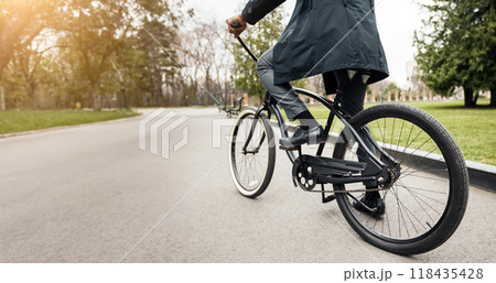 Cropped of African American man in suit riding a bicycle in a park with green trees and grass in the background. Cropped of African American man in suit riding a bicycle in a park with green trees and grass in the background. 118435428