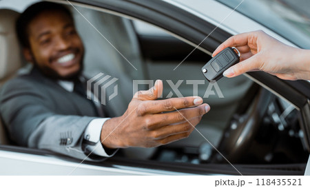 A man sits in the drivers seat of a new car, extending his hand to receive the keys from someone outside the vehicle. He is smiling and appears to be happy and excited about his new car. 118435521