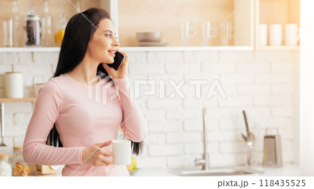A woman in a pink dress is engaged in a phone conversation, holding a cell phone to her ear. She appears to be focused on the call, standing in a casual pose. 118435525