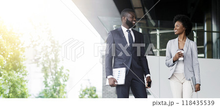 Handsome african businessman and attractive black businesswoman discussing work while walking outdoors Handsome african businessman and attractive black businesswoman discussing work while walking outdoors 118435539