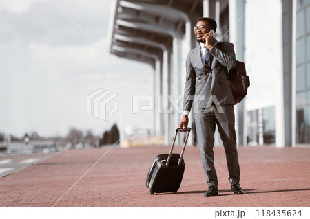 Arriving to Airport. Afro Businessman Talking on Phone and Walking With Luggage 118435624