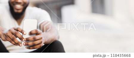 A man with a beard smiles while using a smartphone in a city environment. A man with a beard smiles while using a smartphone in a city environment. 118435668