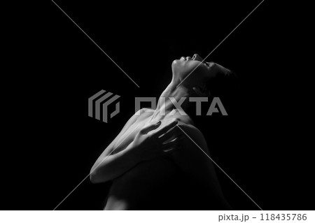 The photo is a black and white portrait of a woman with her head tilted back, looking up. She has her arms around her torso and her face is illuminated by the light from the background. The photo is a black and white portrait of a woman with her head tilted back, looking up. She has her arms around her torso and her face is illuminated by the light from the background. 118435786