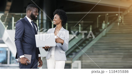 Young african woman pointing finger to laptop screen while standing outdoors with her colleague 118435886