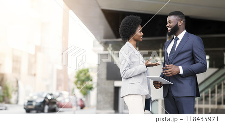 Attractive african american coworkers having pleasant chat while standing against office center, copy space Attractive african american coworkers having pleasant chat while standing against office center, copy space 118435971
