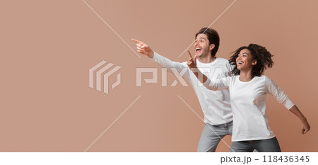 Cool offer. Joyful multiracial couple pointing at copy space and jumping over yellow background in studio, full length shot 118436345