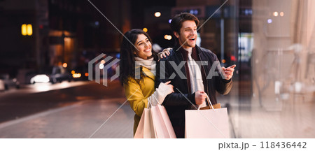 A man and woman are seen casually strolling down the street while holding shopping bags in their hands. A man and woman are seen casually strolling down the street while holding shopping bags in their hands. 118436442