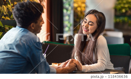 African American guy and girl are seated at a table in a bustling restaurant, engaged in conversation and enjoying their meal together. 118436636