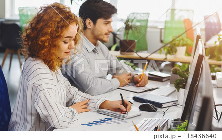 A man and a woman are seated at a desk, focused on their computer screens. They are engaged in work, typing and clicking on the keyboard and mouse respectively. A man and a woman are seated at a desk, focused on their computer screens. They are engaged in work, typing and clicking on the keyboard and mouse respectively. 118436640
