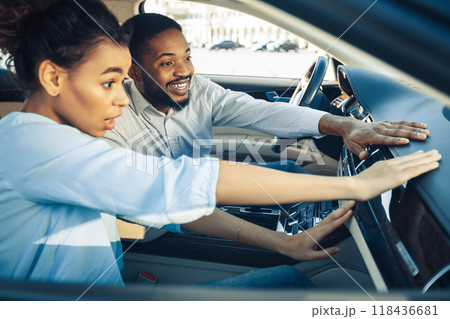 African American woman reaches for the air vent on the dashboard of a car, while the man in the drivers seat looks at her with a smile. African American woman reaches for the air vent on the dashboard of a car, while the man in the drivers seat looks at her with a smile. 118436681
