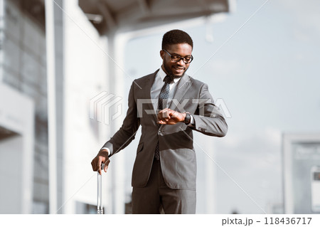 African American man with a suitcase is checking the time at the entrance of a modern airport. The mood is bustling and professional, emphasizing the busy life of a traveler. 118436717