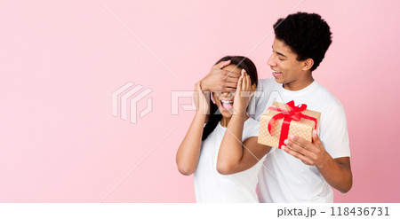 Loving guy closing lady's eyes preparing gift over pink studio background, crop 118436731