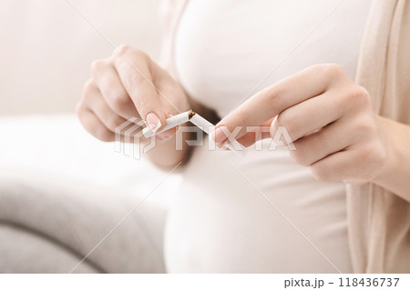 A pregnant woman is seen holding and breaking a cigarette in her hands, indicating her decision to quit smoking for the health of her baby. The setting appears to be a bright, cropped A pregnant woman is seen holding and breaking a cigarette in her hands, indicating her decision to quit smoking for the health of her baby. The setting appears to be a bright, cropped 118436737