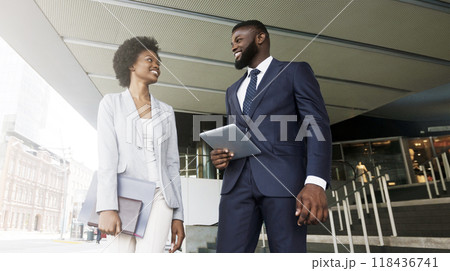 Two smiling african american colleagues discussing new project while going out of office building, copy space 118436741