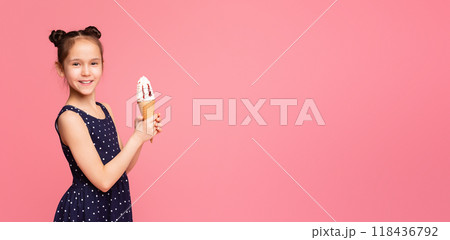 A young girl is holding an ice cream cone in her hand. She looks excited and happy as she enjoys the frozen treat, panorama with copy space A young girl is holding an ice cream cone in her hand. She looks excited and happy as she enjoys the frozen treat, panorama with copy space 118436792