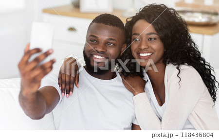 A happy couple takes a selfie together while sitting on a couch in their living room. 118436804
