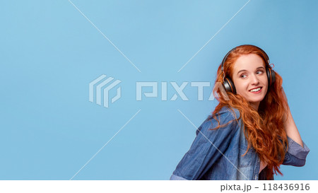 A woman with vibrant long red hair is wearing headphones. She appears to be listening to music or a podcast, immersed in sound, copy space 118436916