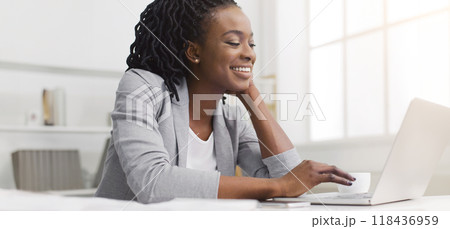 A hardworking African American lady is using her laptop in an office. The mood is productive and professional, with a tidy desk and modern decor, reflecting dedication to her work. A hardworking African American lady is using her laptop in an office. The mood is productive and professional, with a tidy desk and modern decor, reflecting dedication to her work. 118436959