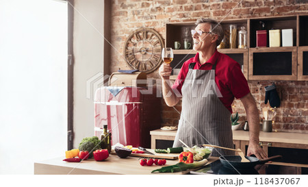 A senior man wearing an apron stands in his kitchen, smiling and holding a glass of wine, looking away from the camera as he enjoys a moment of leisure while preparing a meal A senior man wearing an apron stands in his kitchen, smiling and holding a glass of wine, looking away from the camera as he enjoys a moment of leisure while preparing a meal 118437067