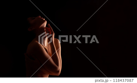 A woman stands in a dimly lit room with her back to the camera, facing towards the right side of the frame. Her body is partially visible against the dark background, copy space 118437087