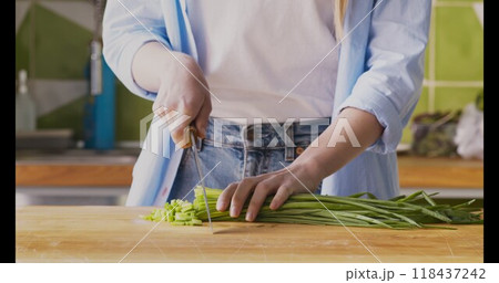 Woman grinding fresh green onions on wooden cutting board in kitchen, closeup. 118437242