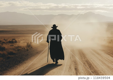 Silhouette of a person in a long coat and hat walking on a dusty road towards distant mountains, with dramatic lighting and dust clouds 118439504