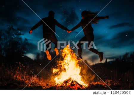 Silhouette of two people holding hands and leaping over a blazing bonfire at night, with sparks flying in a starry sky 118439507