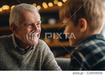 Smiling elderly man in a sweater looking lovingly at his young grandson, with warm lighting and bokeh background suggesting a cozy home setting 118439508