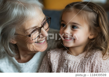 Close-up of a smiling elderly woman with glasses and a young girl with braided hair, sharing a tender moment and displaying intergenerational love 118439509