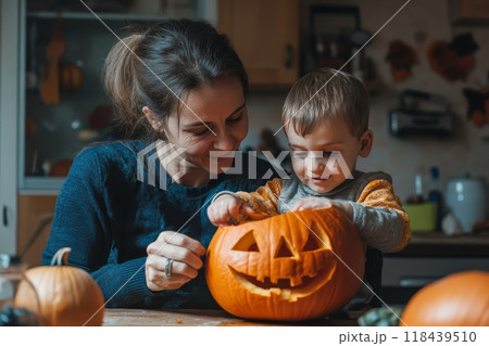 A mother and young boy work together to carve a jack-o'-lantern in a cozy kitchen, showcasing family bonding during autumn festivities 118439510