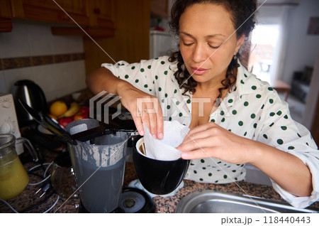 Woman preparing coffee in a cozy kitchen, placing a filter in a coffee machine for a fresh morning brew 118440443