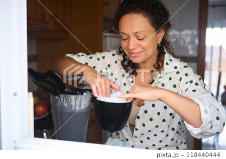 Woman preparing coffee at home using coffee maker, enjoying a peaceful morning routine in a cozy kitchen setting 118440444