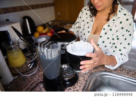 Woman preparing coffee with a filter in a cozy kitchen setting on a relaxing morning with fresh fruit on the counter 118440448