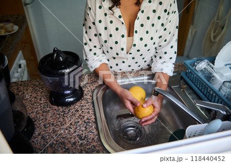 Woman washing fresh oranges at the kitchen sink for healthy juice preparation with a juicer on the countertop 118440452