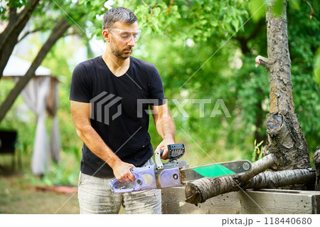 Young man using chainsaw for cutting tree branches at his backyard. 118440680