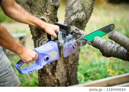 Close-up of man cutting trees using electrical chainsaw in motion 118440684