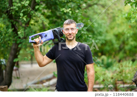 Smiling man with electric chainsaw posing in his garden Smiling man with electric chainsaw posing in his garden 118440688