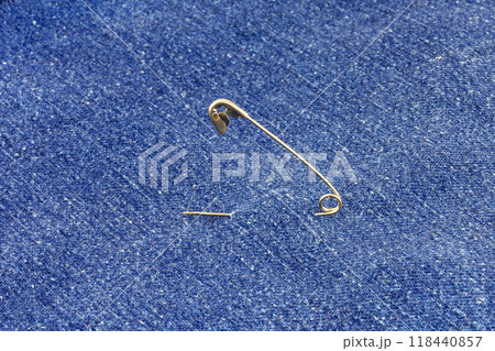 Blue denim pierced by a metal pin. Metal pin threaded through the blue denim 118440857