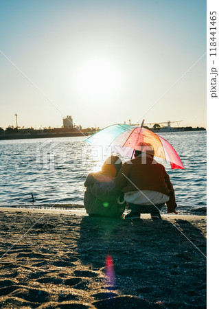 海辺の夕日に照らされるカラフルの相合傘をした男の子と女の子 118441465