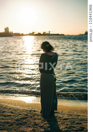 海で夕日を眺めながら俯く女性 118441966