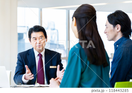 ミドルの夫婦に営業するビジネスマン　撮影協力：学校法人電波学園　東京電子専門学校 118443285