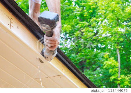 An employee cuts off existing vinyl soffit plastic panels to given size on new home facade ceiling An employee cuts off existing vinyl soffit plastic panels to given size on new home facade ceiling 118444075