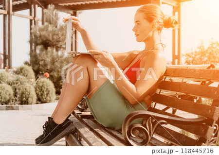 Woman, Bench, Park - A woman wearing a red tank top and green shorts sits on a wooden bench in a park and reads a book. Woman, Bench, Park - A woman wearing a red tank top and green shorts sits on a wooden bench in a park and reads a book. 118445716