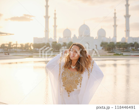 Travel to the United Arab Emirates, Abu Dhabi. Woman in white Arabic dress looking at Sheikh Zayed Great white mosque. famous Abu Dhabi sightseeing. Travel to the United Arab Emirates, Abu Dhabi. Woman in white Arabic dress looking at Sheikh Zayed Great white mosque. famous Abu Dhabi sightseeing. 118446491