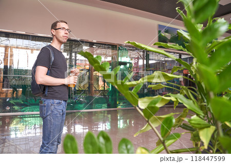 Man with backpack drinking orange juice in indoor shopping mall with greenery Man with backpack drinking orange juice in indoor shopping mall with greenery 118447599