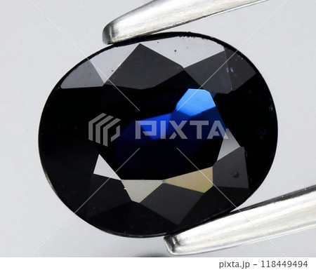Brilliantly Faceted Dark Blue Oval Gemstone Held by Silver Tweezers Brilliantly Faceted Dark Blue Oval Gemstone Held by Silver Tweezers 118449494